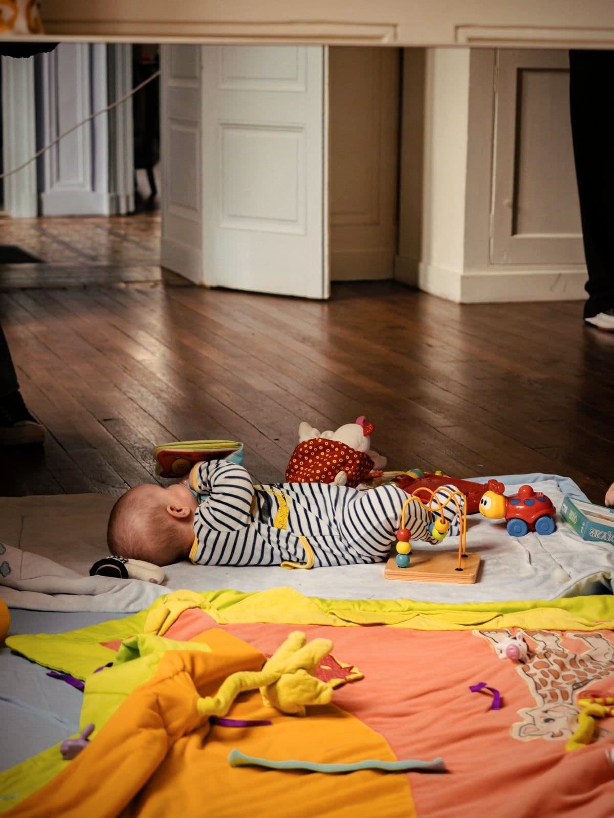 Un bébé allongé sur un tapis d’éveil, entouré de ses jouets, dans le salon d’une des maisons.